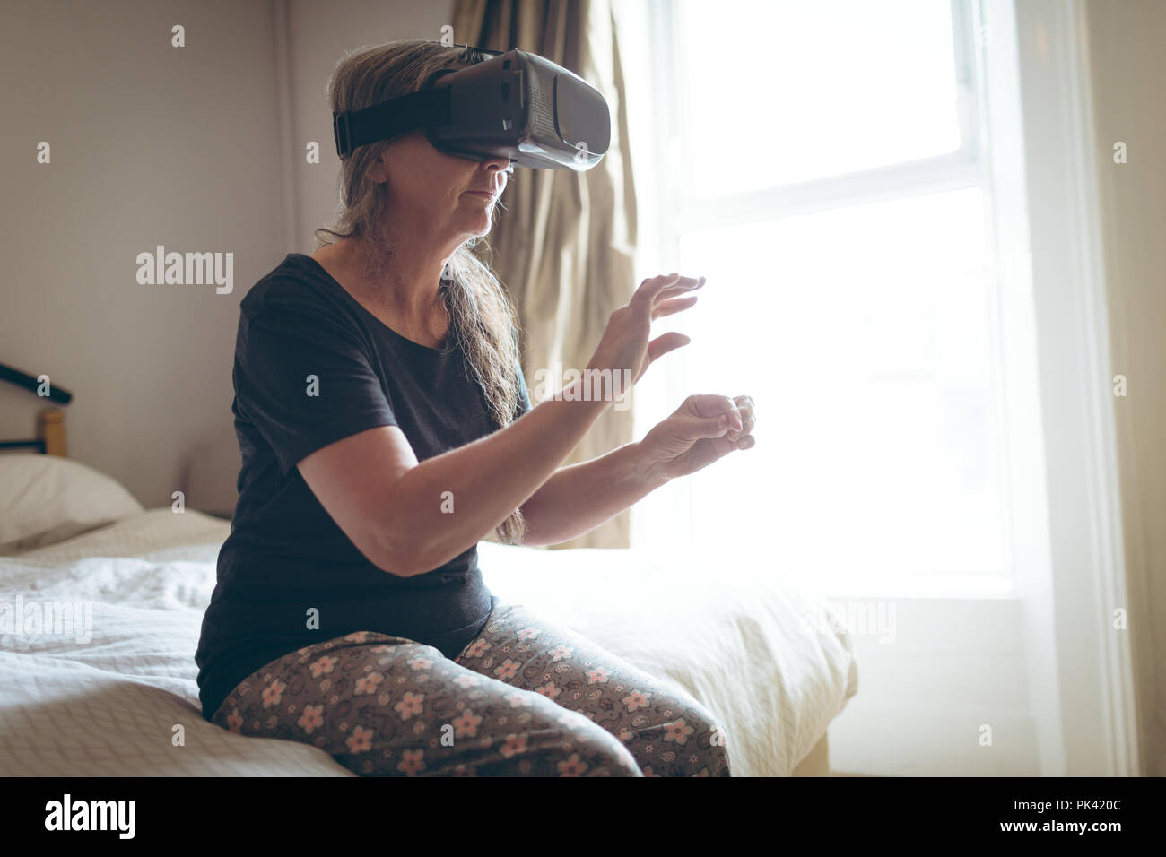 Senior donna utilizzando la realtà virtuale auricolare in camera da letto Foto Stock