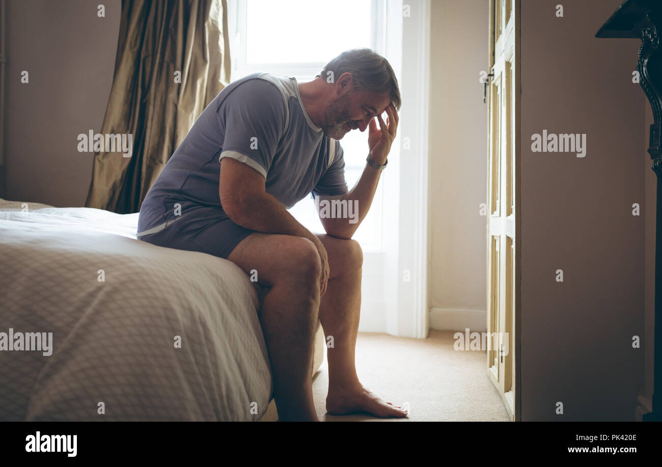 Senior uomo seduto sul letto in camera da letto a casa Foto Stock