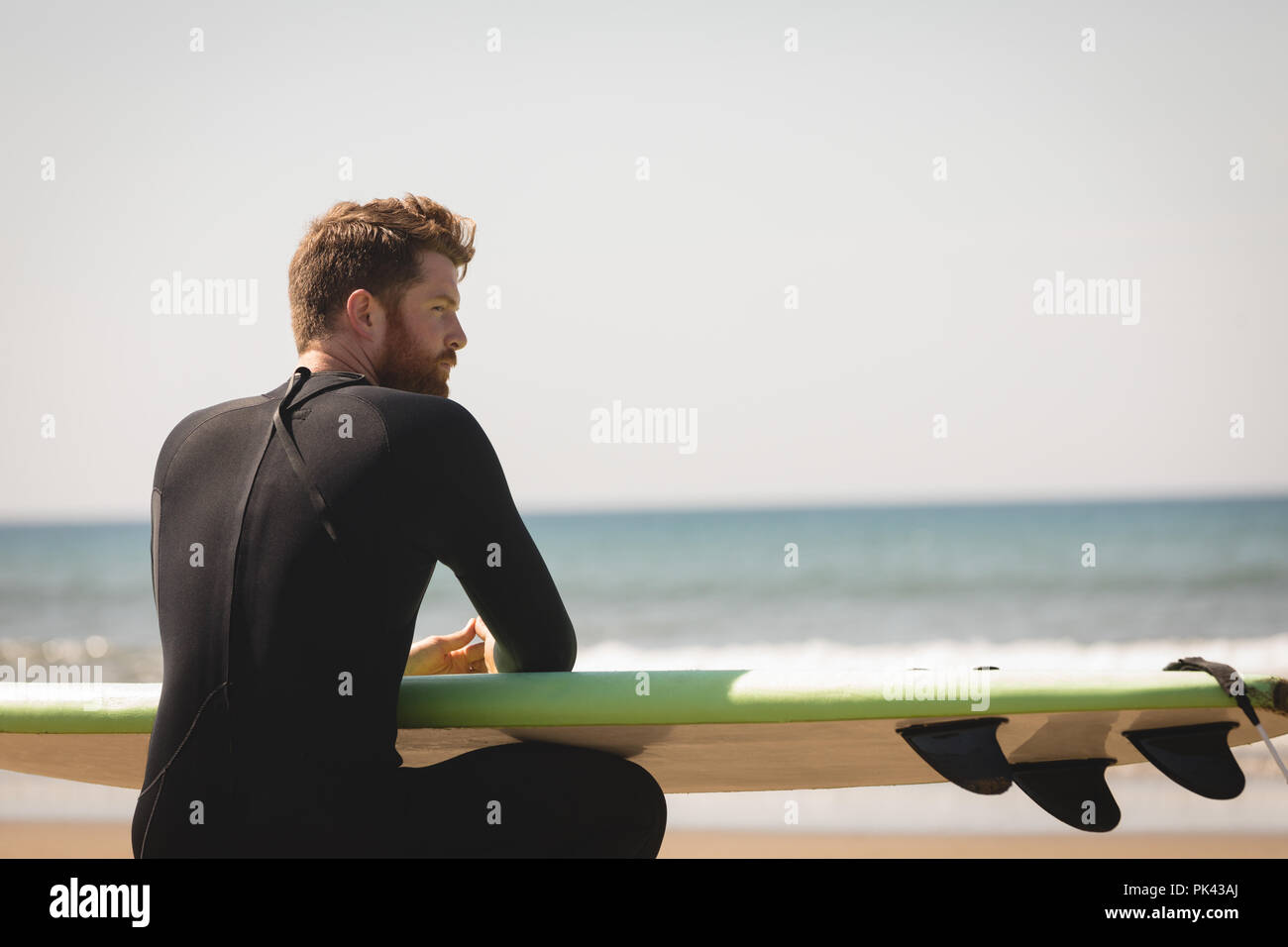 Surfer con tavola da surf seduto alla spiaggia Foto Stock