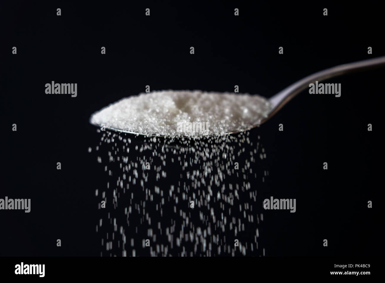 Studio Immagine di un metallo cucchiaio zucchero versatore isolata su uno sfondo nero in cucina dolce zucchero dipendenza malsana dieta sovrappeso e obesità co Foto Stock