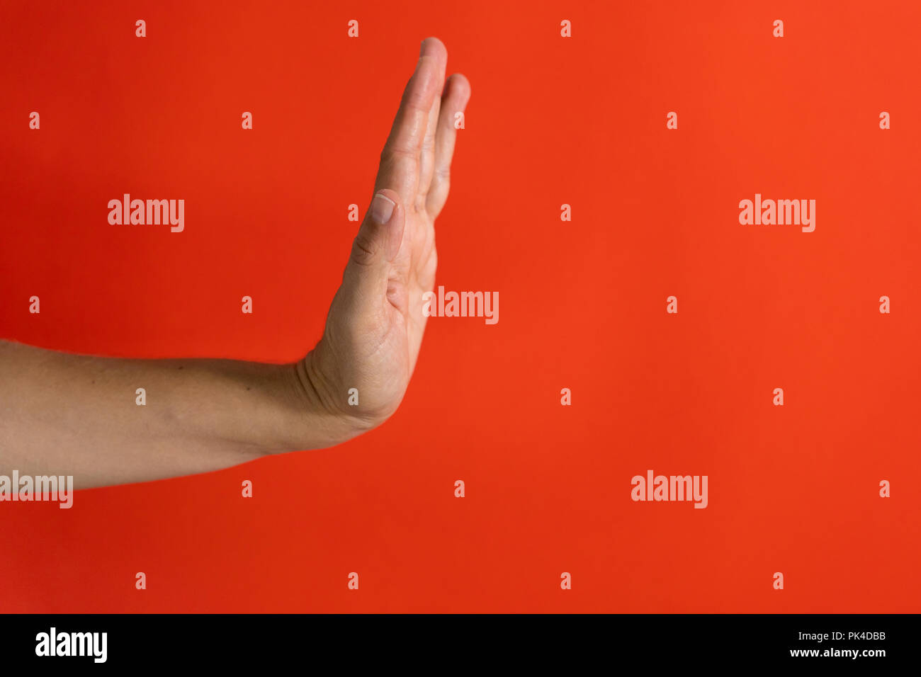 Studio foto di una donna che mostra a mano arrestare il gesto e segno isolato su uno sfondo di colore rosso a respingere il concetto di arresto. Foto Stock