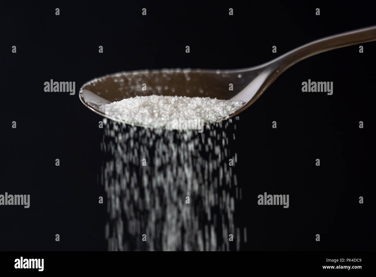 Studio Immagine di un metallo cucchiaio zucchero versatore isolata su uno sfondo nero in cucina dolce zucchero dipendenza malsana dieta sovrappeso e obesità co Foto Stock