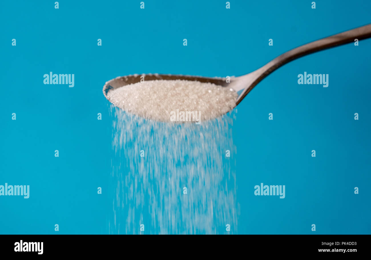 Studio Immagine di un metallo cucchiaio zucchero versatore isolata su uno sfondo blu in cucina dolce zucchero dipendenza malsana dieta sovrappeso e obesità con Foto Stock