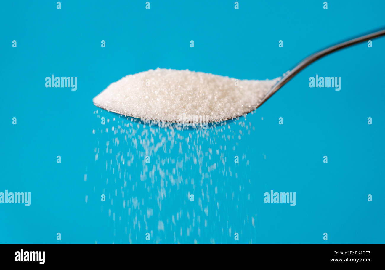 Studio Immagine di un metallo cucchiaio zucchero versatore isolata su uno sfondo blu in cucina dolce zucchero dipendenza malsana dieta sovrappeso e obesità con Foto Stock
