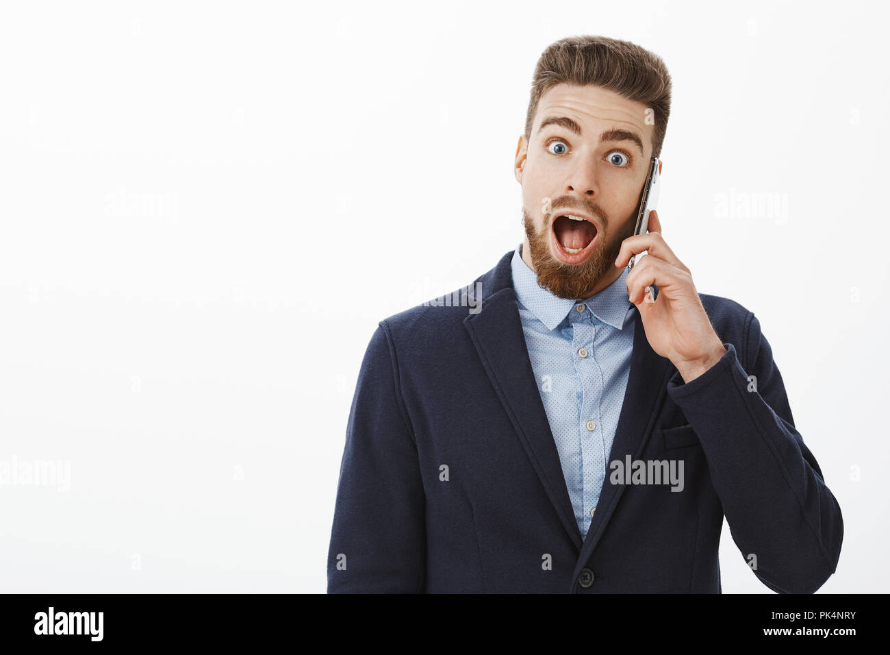 Wow la mia azienda ha sollevato un altro milione. Entusiasti e stupiti di buona cercando maschio maturo con gli occhi blu e la barba in abito formale holding smartphone vicino all orecchio learning scioccanti, caduta di sorpresa a ganascia Foto Stock