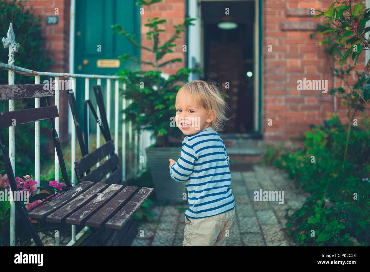 Un ridere toddler è giocare in giardino nella parte anteriore della sua casa Foto Stock