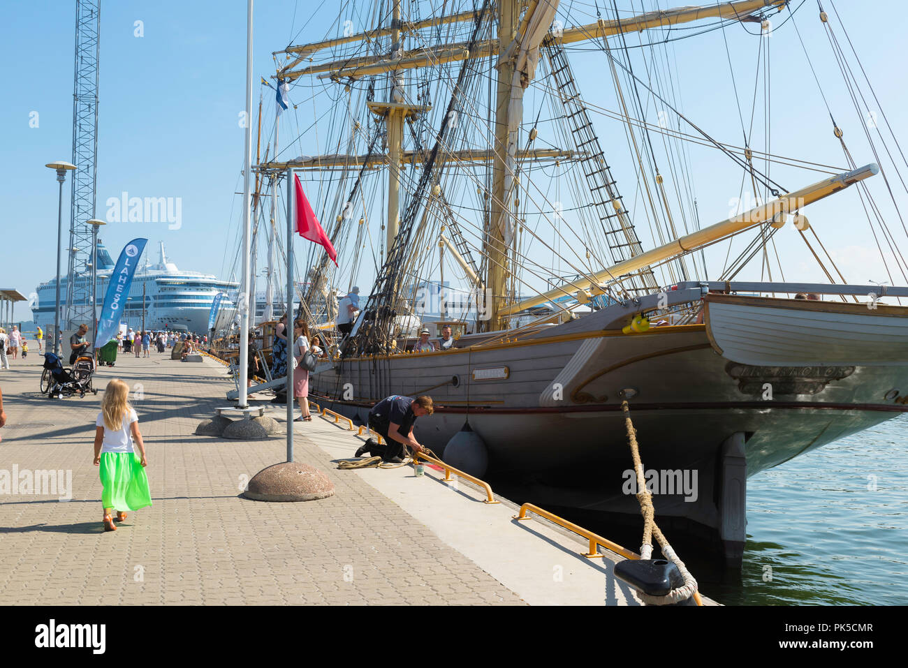 Bambino nave porto, vista posteriore di un piccolo bambino in un mantello verde camminare al fianco di un palazzo del XIX secolo nave a vela nel porto di Tallinn su un giorno d'estate, in Estonia. Foto Stock