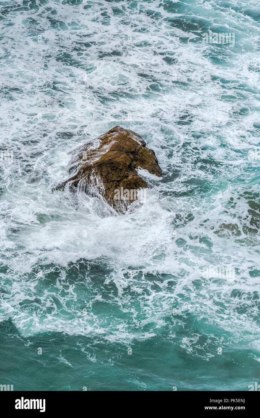 Mare increspato turbinano intorno una roccia.; Foto Stock