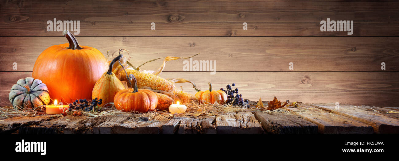 Sfondo del ringraziamento - Zucche con il tutolo di mais e candele su tavola in legno rustico Foto Stock