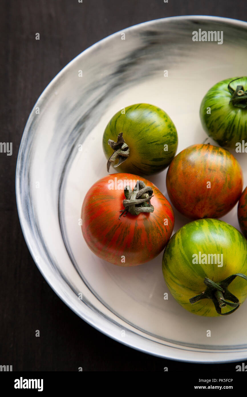 Cimelio di freschi pomodori in un bianco e grigio ciotola in marmo su sfondo nero Foto Stock