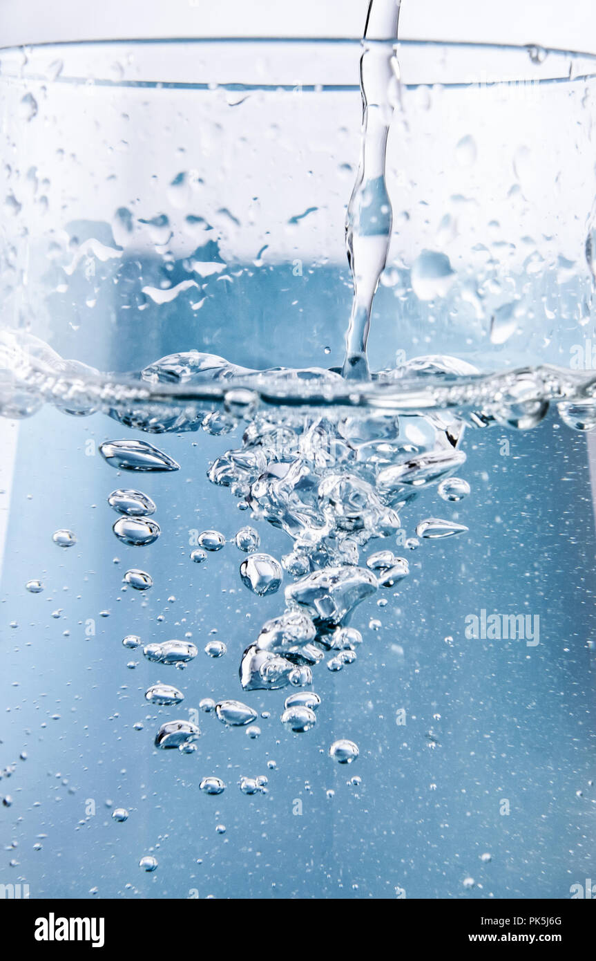 Azione close up (macro) colpo di azzurro acqua potabile che viene versato in un bicchiere con ossigeno formando bolle e in aumento. Foto Stock