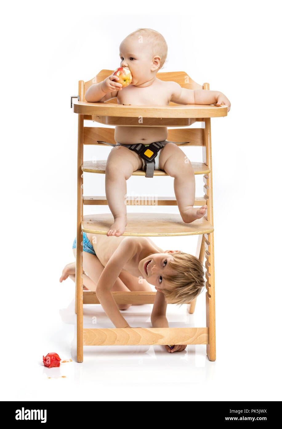 Baby girl seduto nella sedia alta e squisito, ragazzo di età prescolare nascondere sotto la pedana. I fratelli giocando al momento dei pasti. Foto Stock
