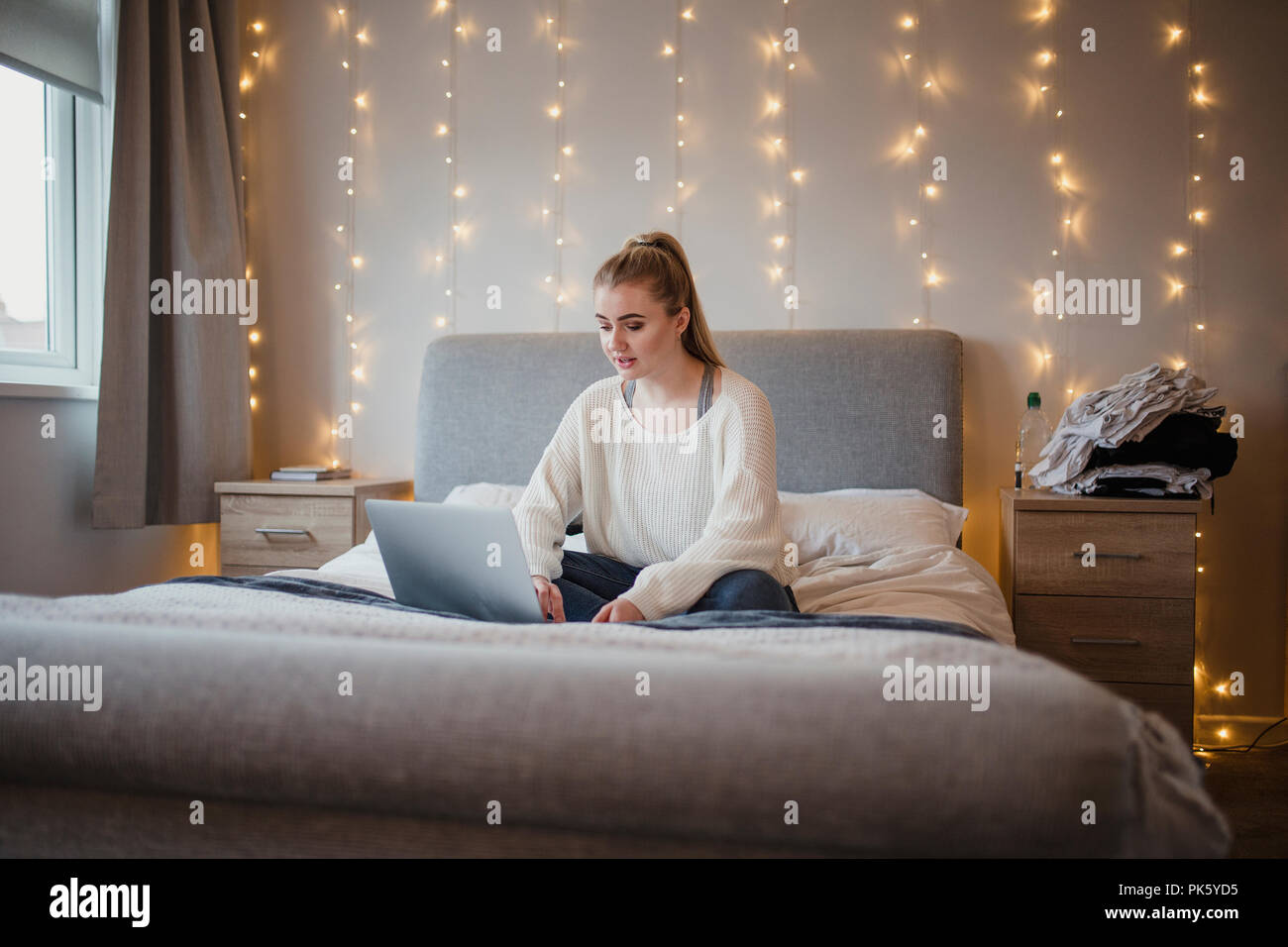 Giovane donna è seduta sul suo letto tramite un computer portatile. Foto Stock