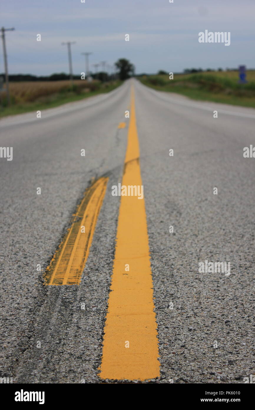 Guardando verso il centro della linea gialla di una retta e una lunga strada di campagna nelle zone rurali a Marengo, Illinois, McHenry County. Foto Stock