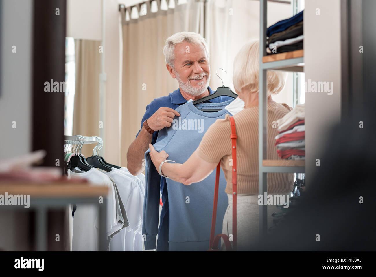 Gioioso uomo anziano mantenendo elegante pullover al suo petto in negozio per lo shopping Foto Stock