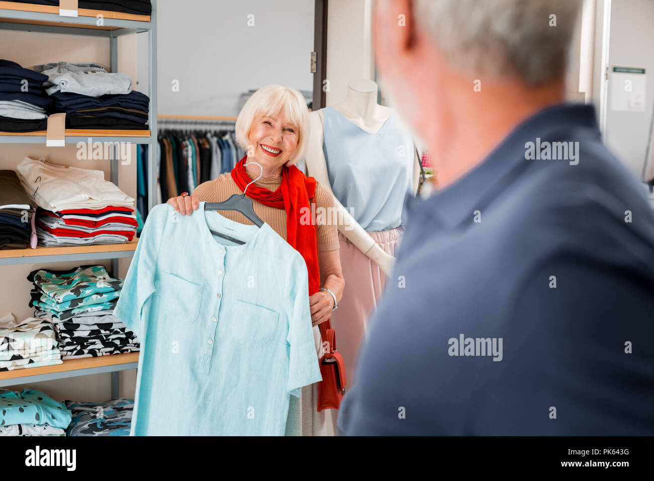 Adorabili dai capelli grigi donna accettando complimenti dal venditore concernenti il suo abito scelto Foto Stock