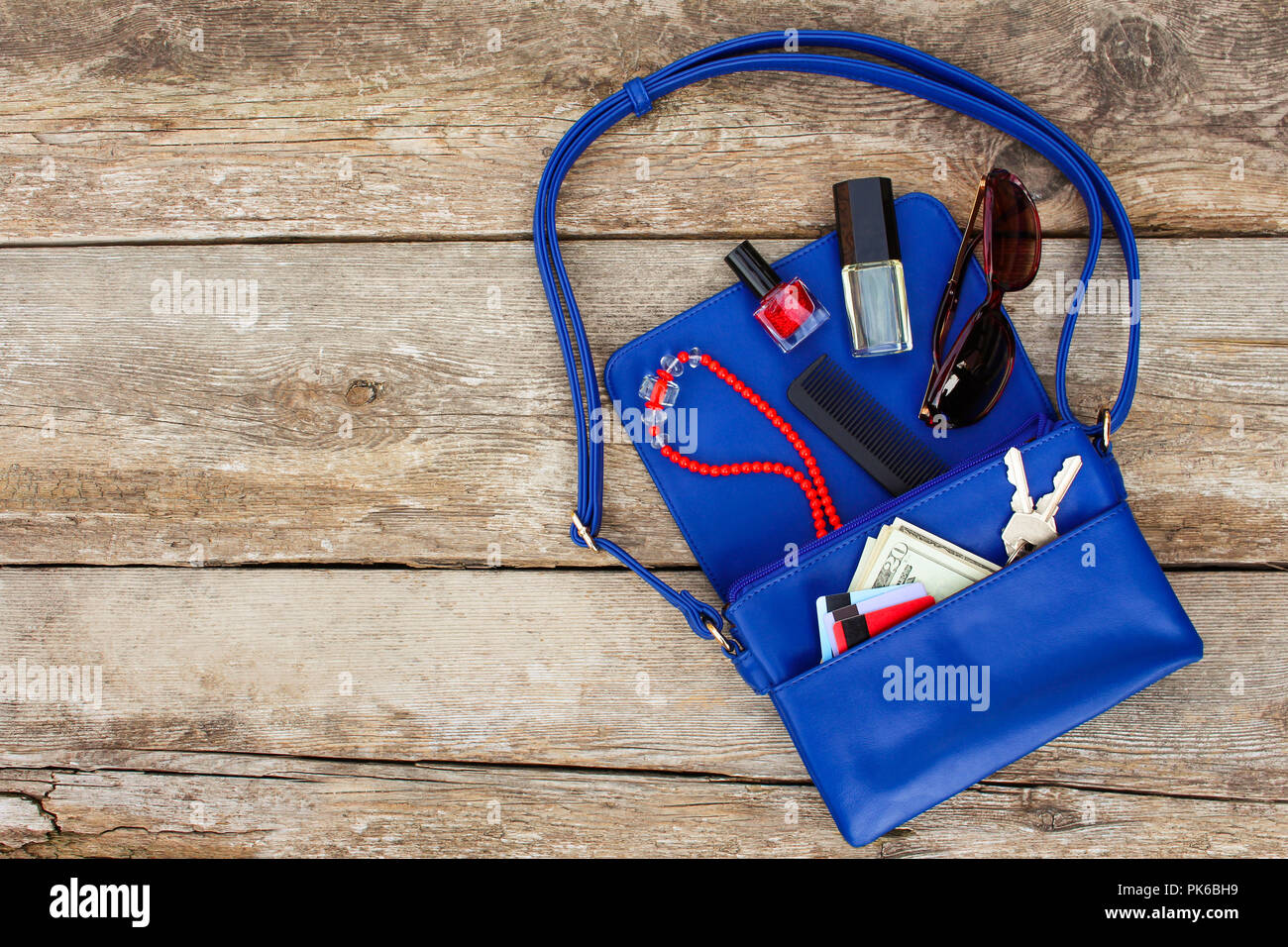 Cose da aprire lady borsa. Cosmetici, soldi e donna accessori è caduto fuori borsa blu. Vista dall'alto. Foto Stock