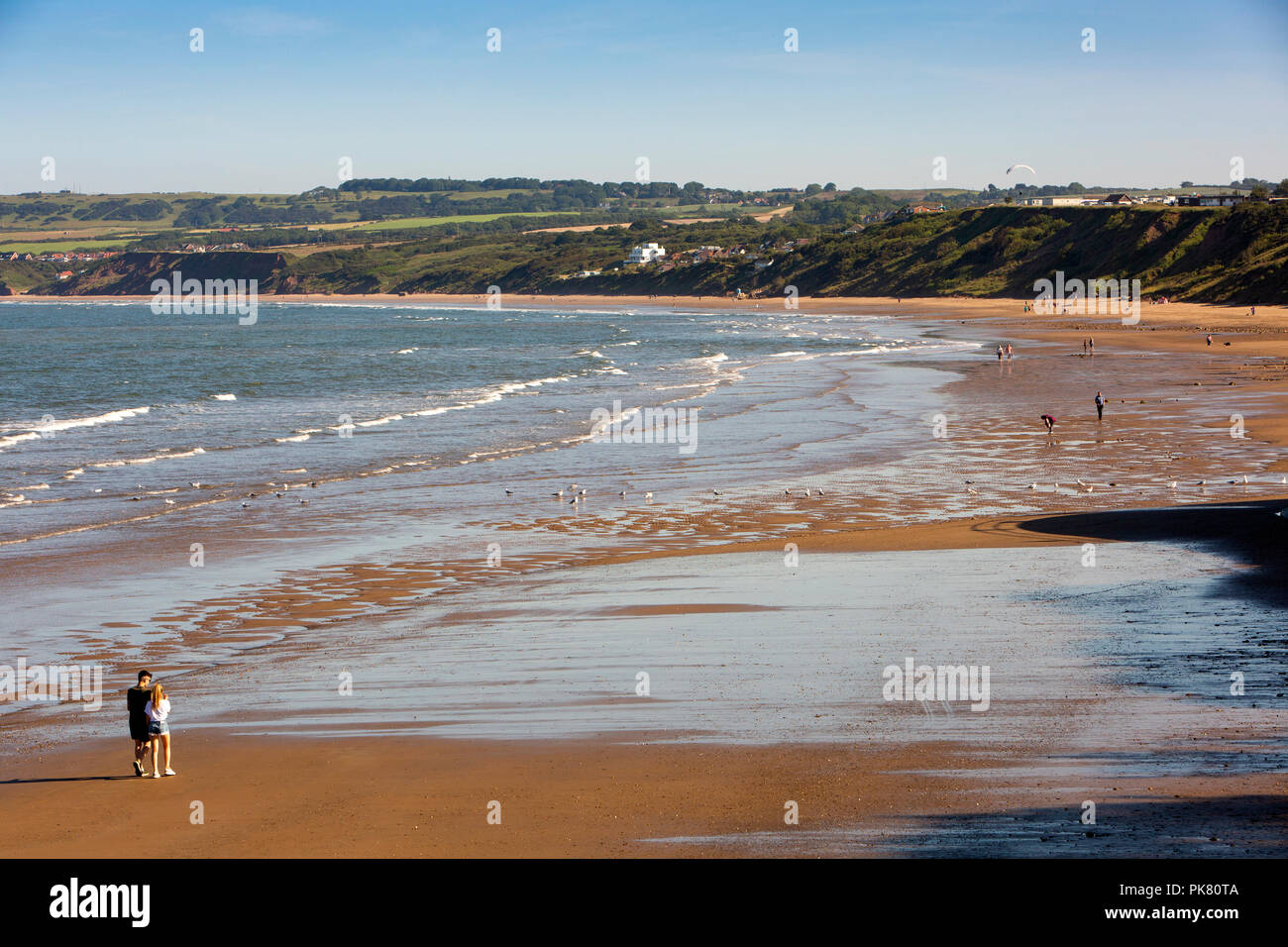 Regno Unito, Inghilterra, Yorkshire, Filey, i visitatori a camminare su Muston Sands Beach a bassa marea nella luce del sole Foto Stock