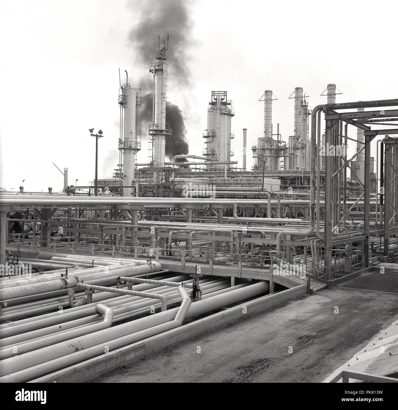 Anni sessanta, storico, vista esterna di una gigantesca raffineria di petrolio nel deserto in Arabia Saudita, che mostra una massa di oleodotti e fiamme o torri di masterizzazione. Foto Stock