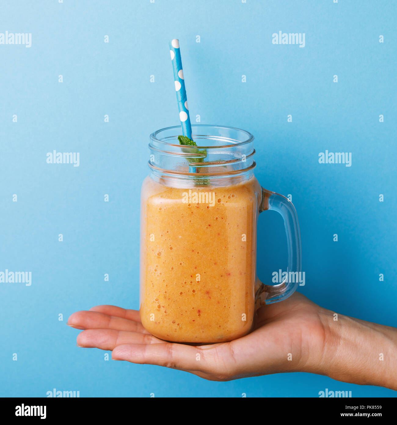 I frullati preparati da un melone maturo in un vasetto di vetro con menta su uno sfondo blu. Bere in piedi sul palmo di un uomo Foto Stock