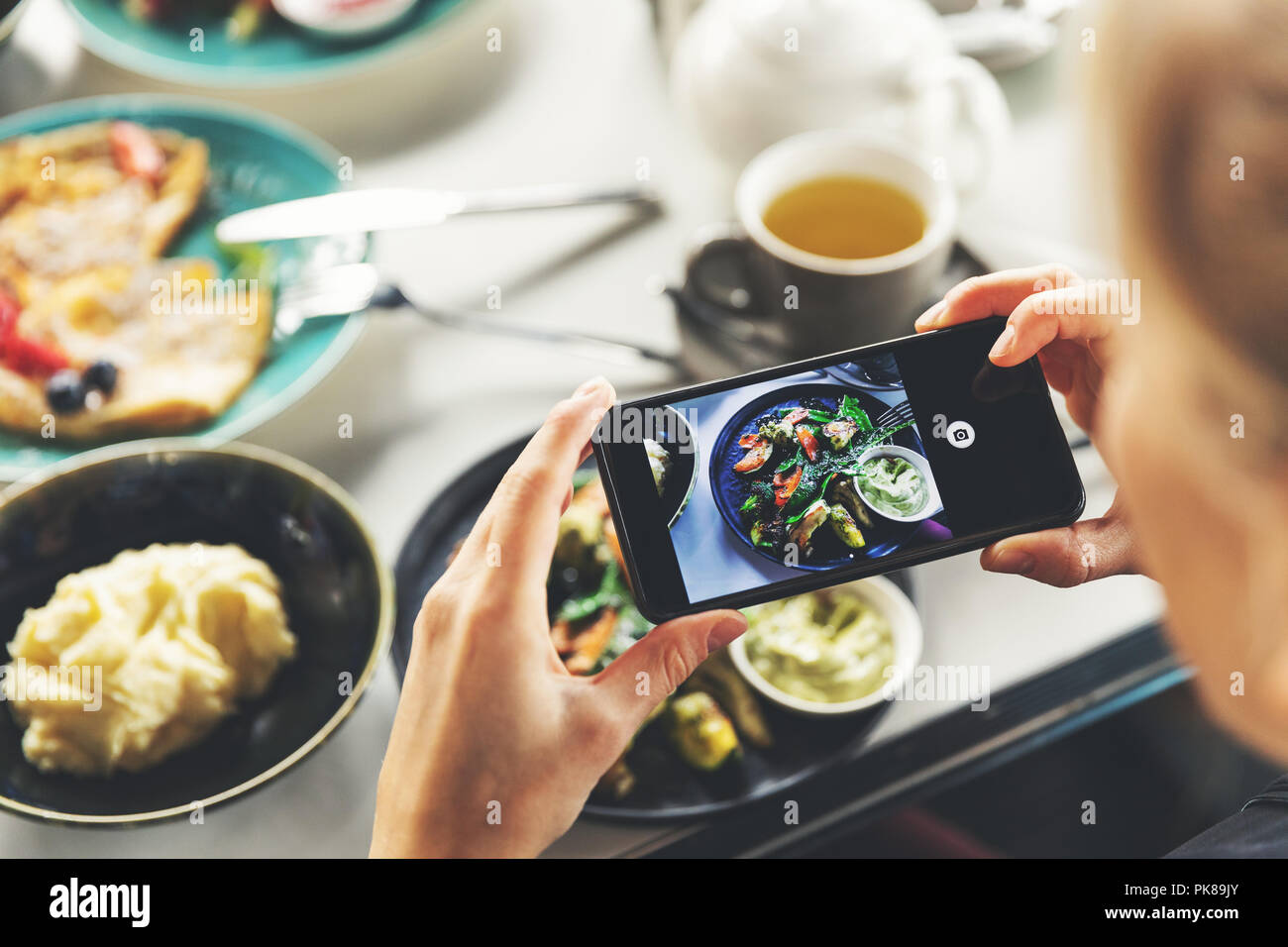 Donna con smart phone di scattare una foto di cibo al ristorante Foto Stock