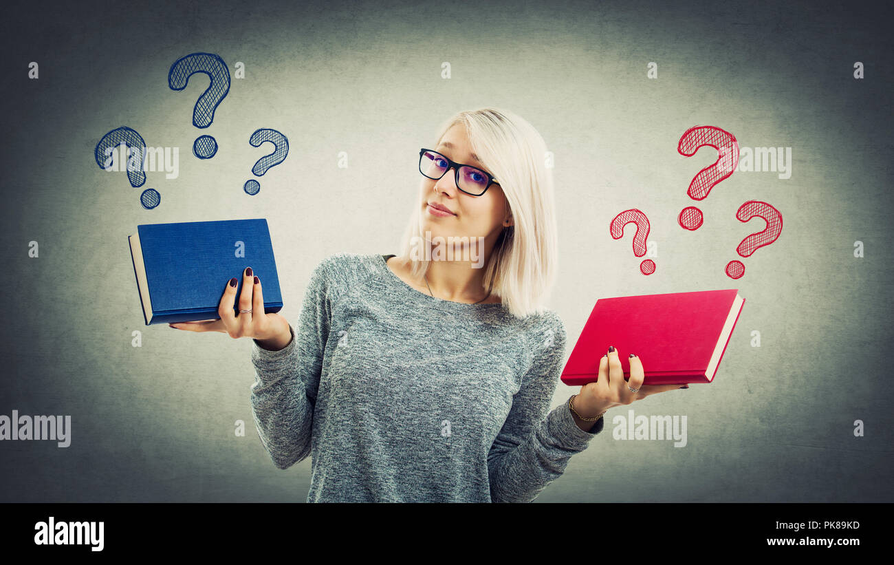 Confuso studente giovane ragazza con due diversi libri deve scegliere tra rosso e blu. Il dubbio e la scelta giusta del concetto. A sinistra o a destra questione whi Foto Stock