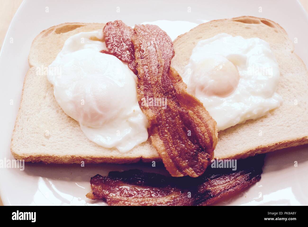 Le uova in camicia con croccante di pancetta su bianco unbuttered toast Foto Stock