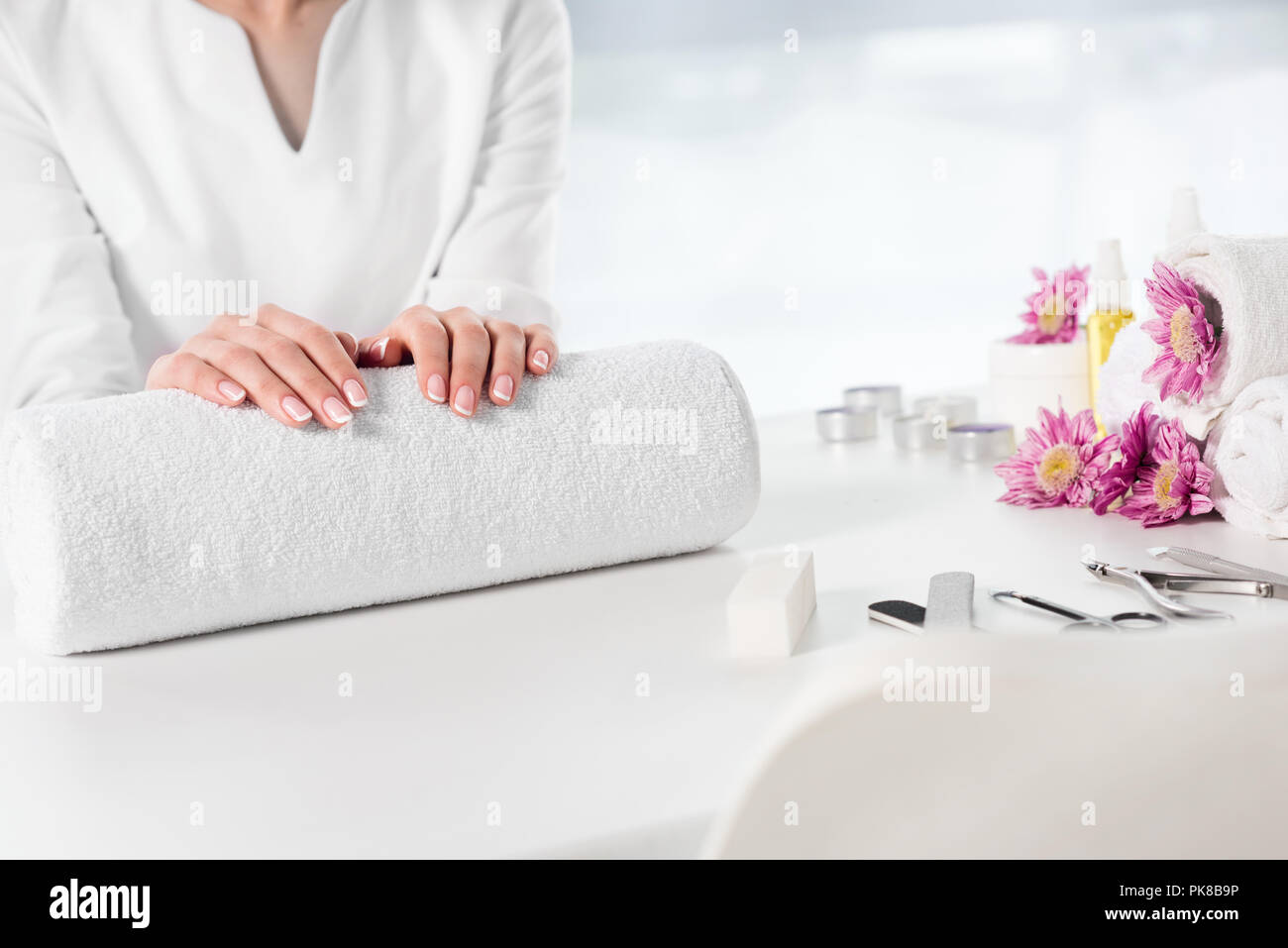 Immagine ritagliata della donna tenendo le mani a tavola con gli asciugamani, fiori, candele, aroma le bottiglie di olio e di strumenti per la manicure nel salone di bellezza Foto Stock