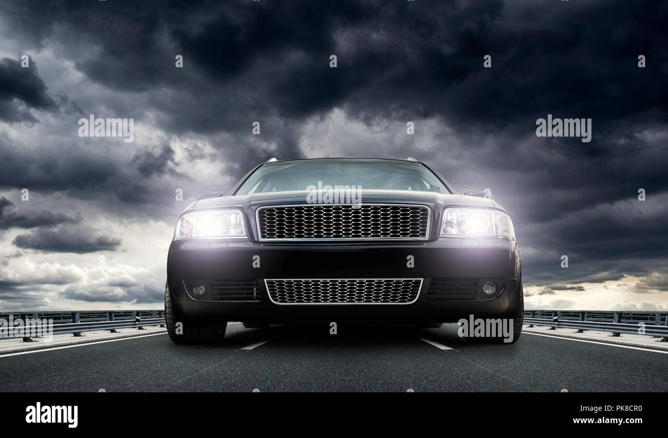 Un potente vettura con luci su cavalletti sull'autostrada al tramonto contro un cielo drammatico. Foto Stock