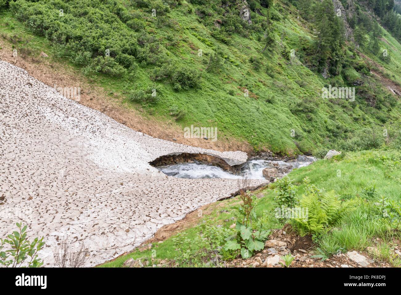 Resti della copertura di ghiaccio e neve coprono oltre un torrente di montagna in estate, Austria Foto Stock