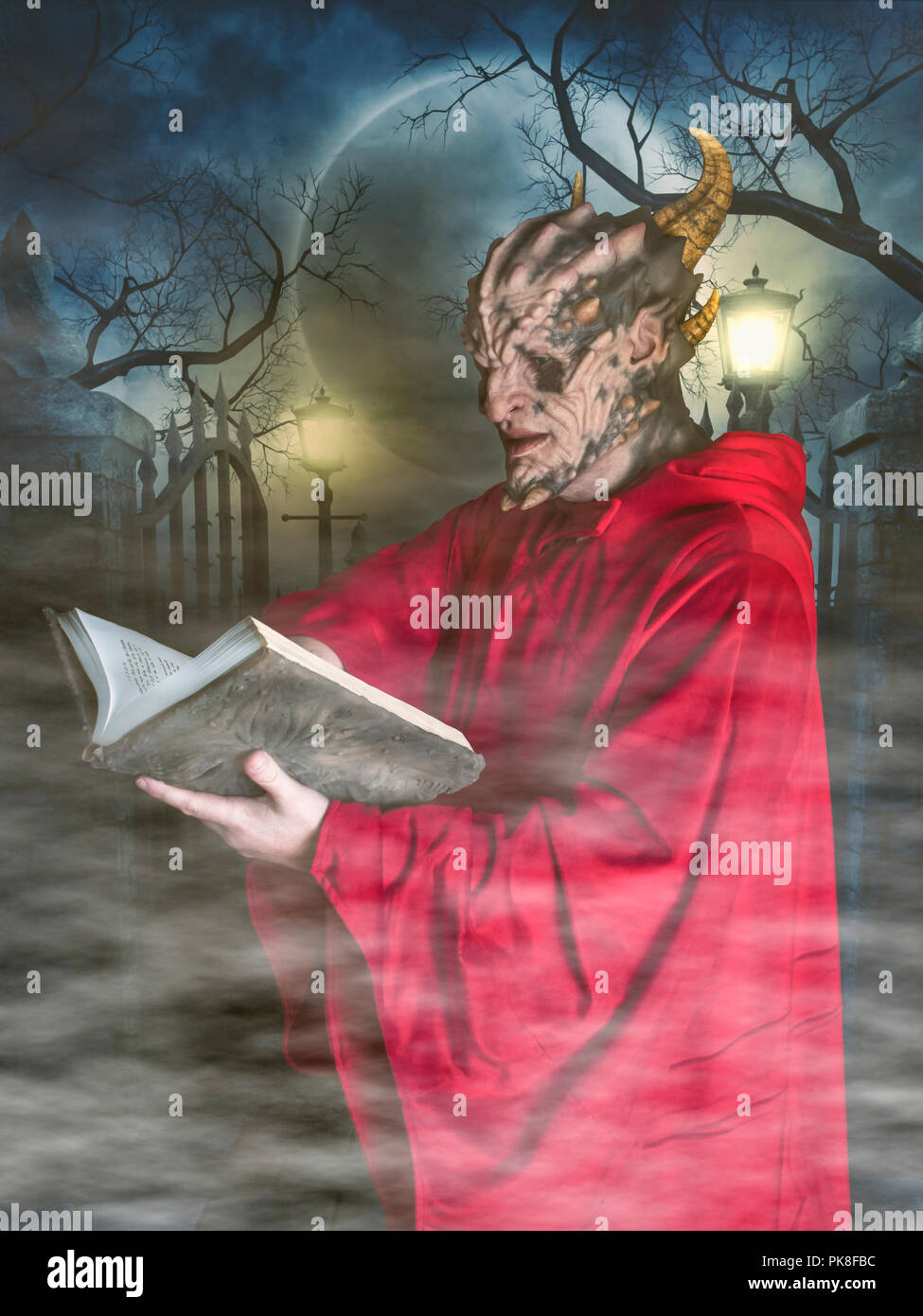 Costume di halloween demon cultista abito rosso con cappuccio la lettura del necronomicon grimoire libro in un cimitero di nebbia di scena a notte monster Foto Stock