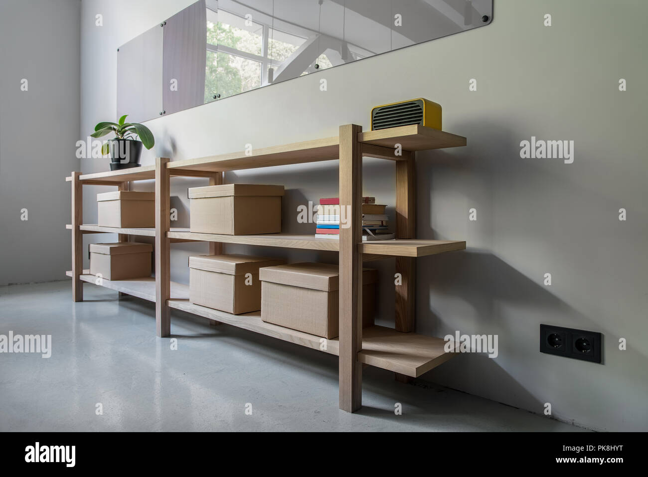 Interno in un ufficio con pareti grigie e un pavimento lucido. Ci sono ripiani in legno con scatole di cartone, pianta verde, libri e un altoparlante giallo, di cinghiale Foto Stock