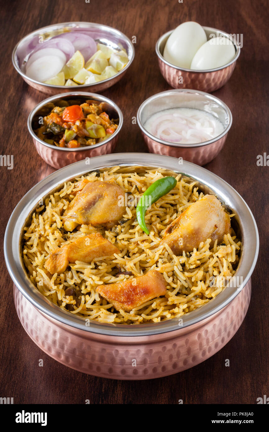 Primo piano vista dalla cima di delizie indiane biryani di pollo servito in autentici utensili in rame con insalata (raita), con sugo di carne e uova. Luce naturale. Foto Stock