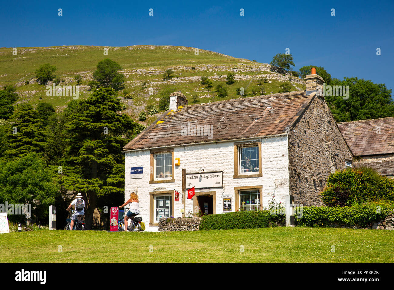 Regno Unito, Yorkshire, Wharfedale, Buckden, ciclisti su biciclette elettriche passando i negozi del villaggio shop Foto Stock