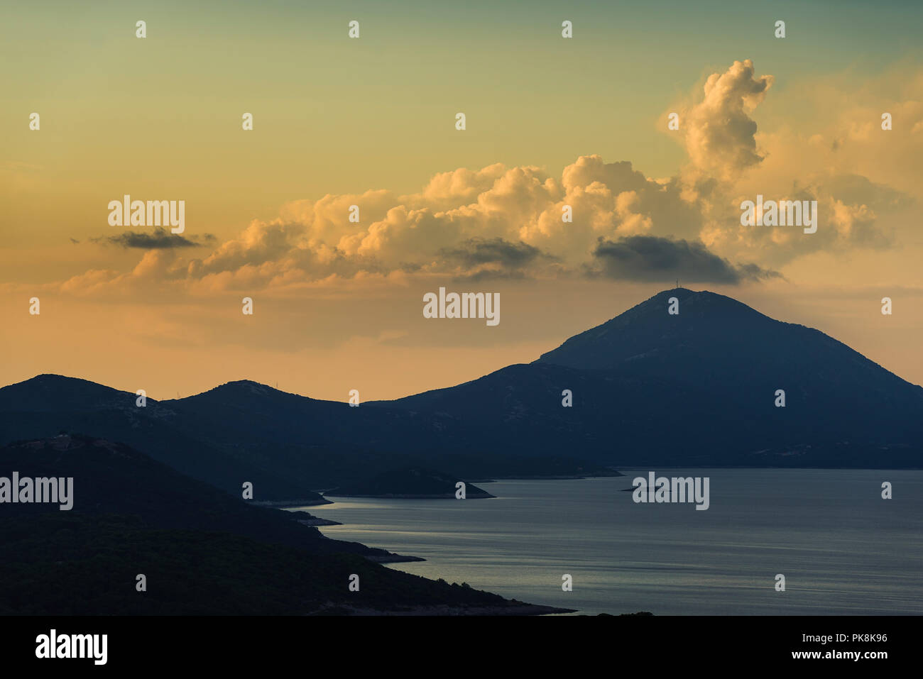 La montagna Osoršćica e la costa dell'isola di Lošinj nella parte anteriore del cumulus nubi nel incandescente luce della sera prima del tramonto, baia di Kvarner, Croazia Foto Stock
