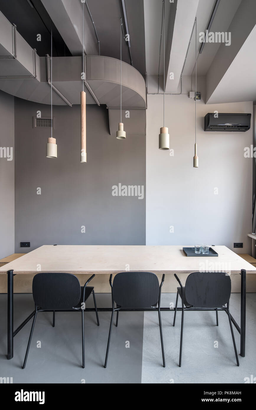 Sala riunioni in un ufficio in stile loft con pareti di colore grigio. Vi è un ampio tavolo di legno con tray nero con gli occhiali, tre sedie scuro, diversi han Foto Stock