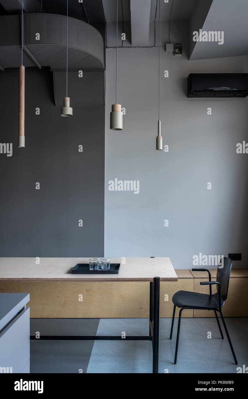 Bella camera in un ufficio in stile loft con pareti di colore grigio. Vi è un ampio tavolo di legno con tray nero con gli occhiali, scuro sedia, differenti beige pendenti Foto Stock