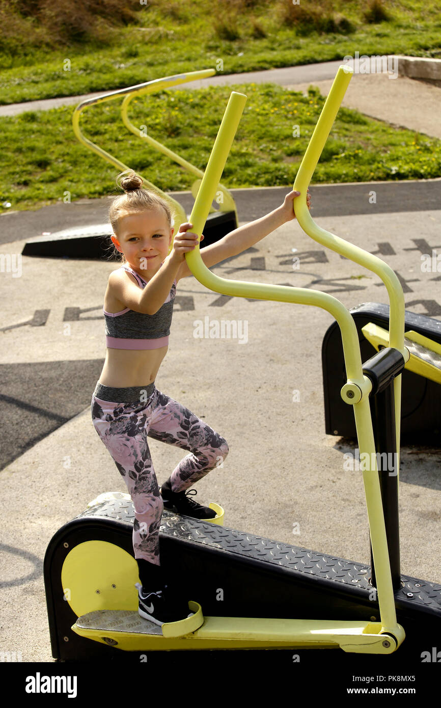 6 anno vecchia ragazza, su un cross trainer macchina in un libero di utilizzare outdoor area fitness Foto Stock