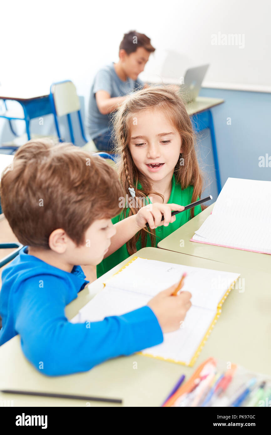 Ragazza aiuta un ragazzo a scuola elementare insegnamento durante la scrittura Foto Stock