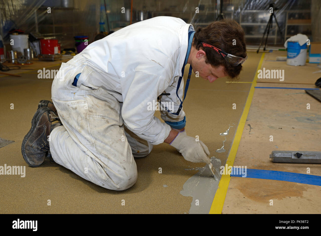 Tradesman pittura bordo del pavimento prima linea prodotto epossidico è utilizzato in un edificio industriale Foto Stock