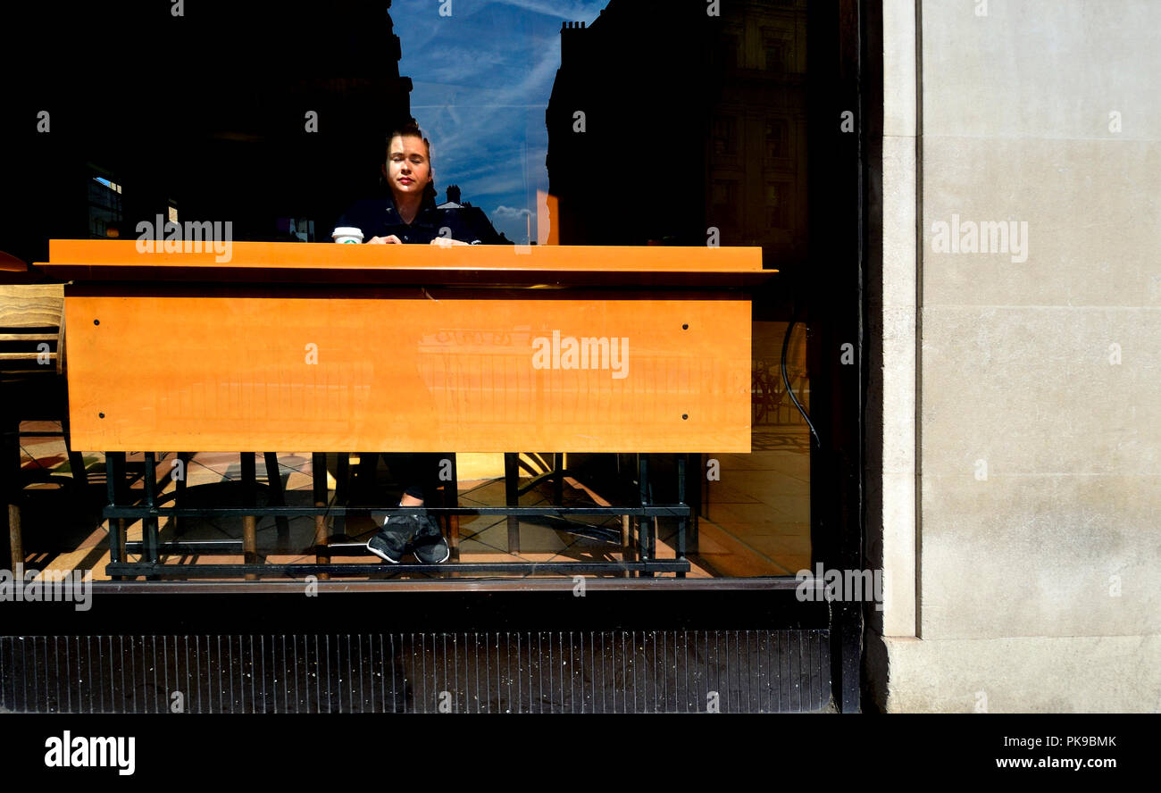 Londra, Inghilterra, Regno Unito. Donna seduta da sola nella vetrina di un negozio di caffè Foto Stock