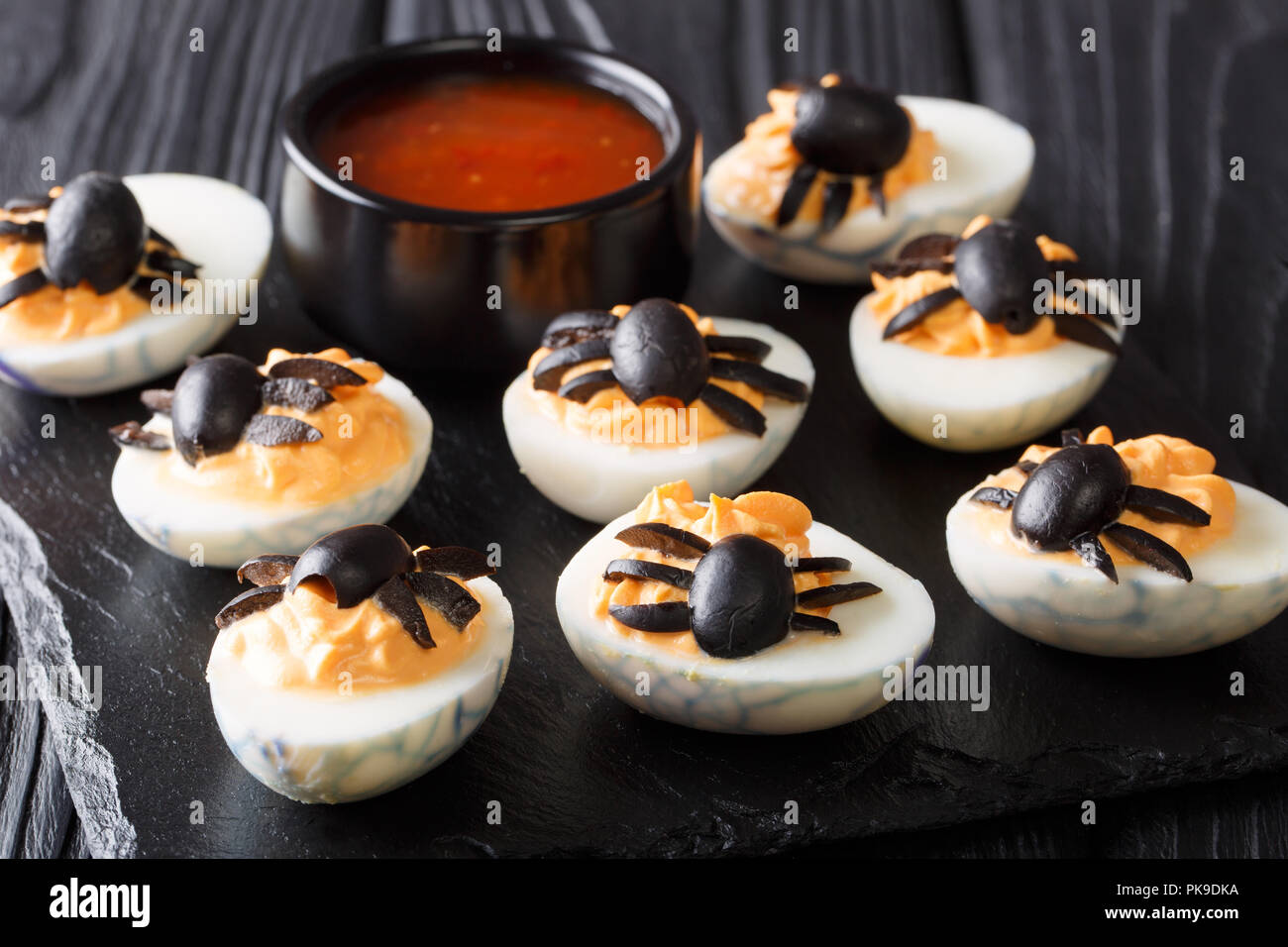 Festive Halloween antipasto: dimezzato deviled uova decorate con olive ragni close-up servita con ketchup su una tavola nera orizzontale. Foto Stock