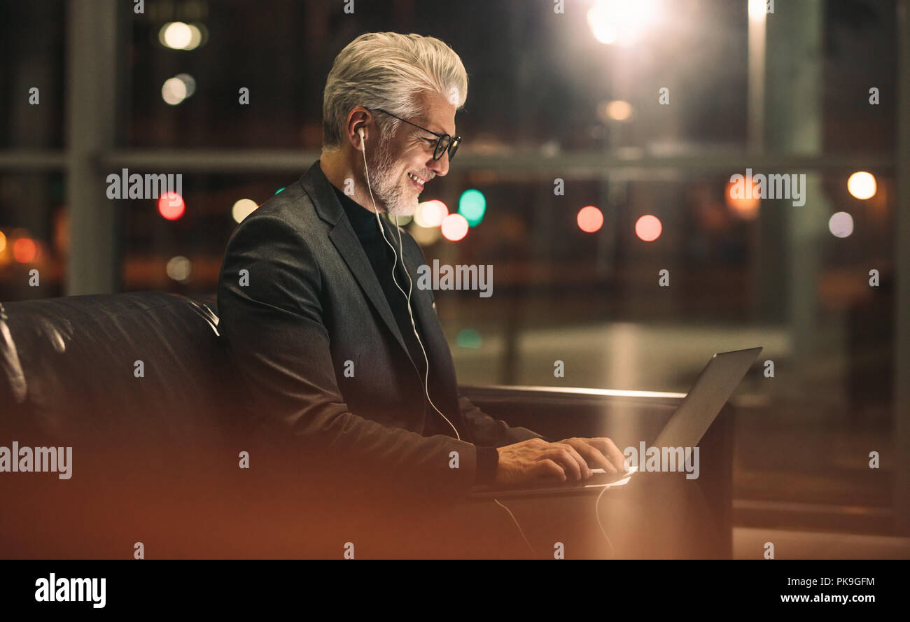 Felice uomo maturo lavora fino a tardi in ufficio. Uomo d affari con computer portatile in ufficio lobby. Foto Stock