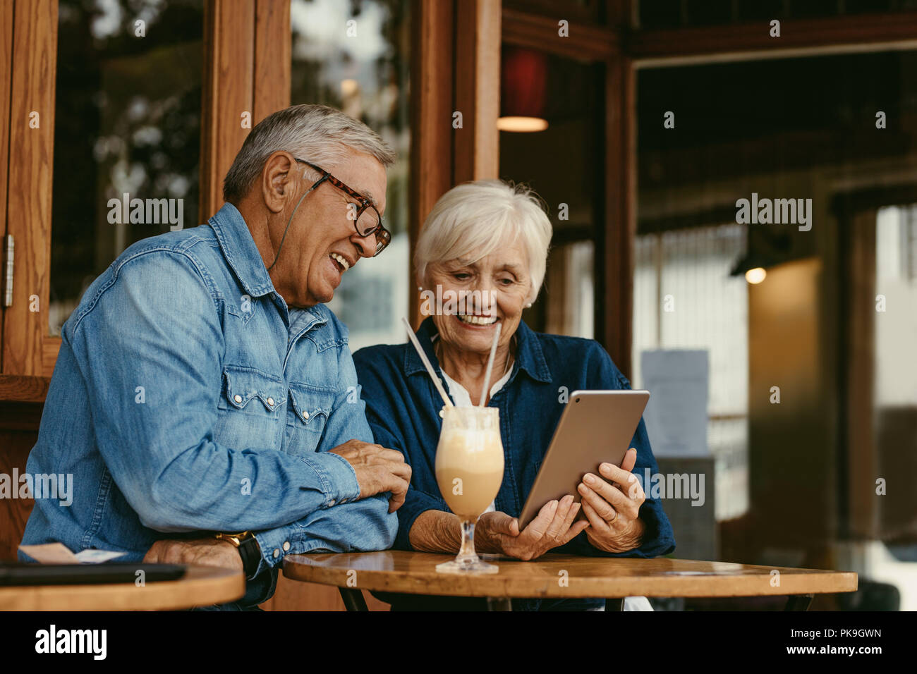 Allegro coppia senior seduti al tavolo del bar e guardando a tavoletta digitale. Senior l uomo e la donna seduta al coffee shop utilizzando tablet pc. Foto Stock