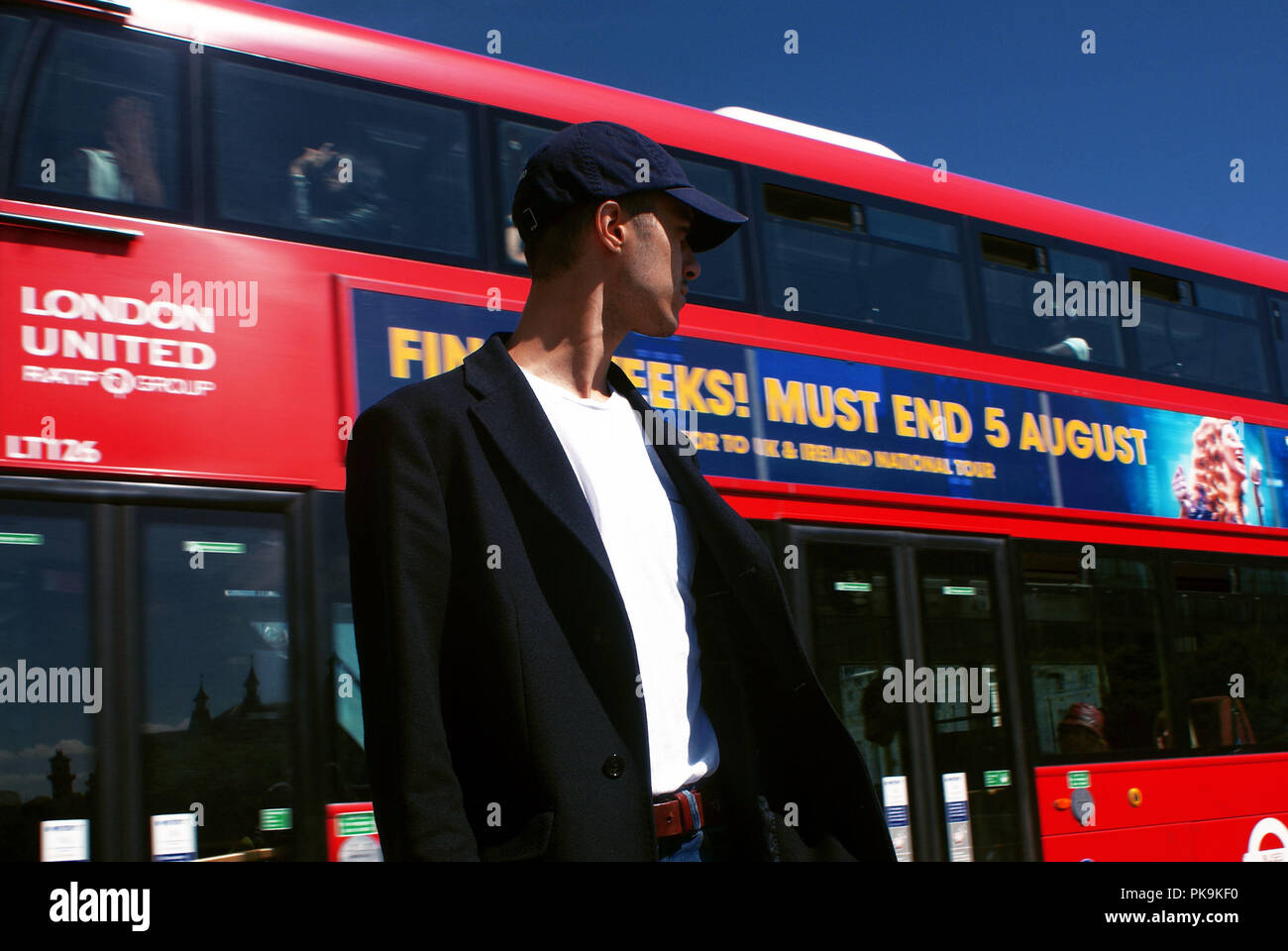 Giovane uomo in piedi accanto a un bus in movimento in abbigliamento casual in una città Foto Stock