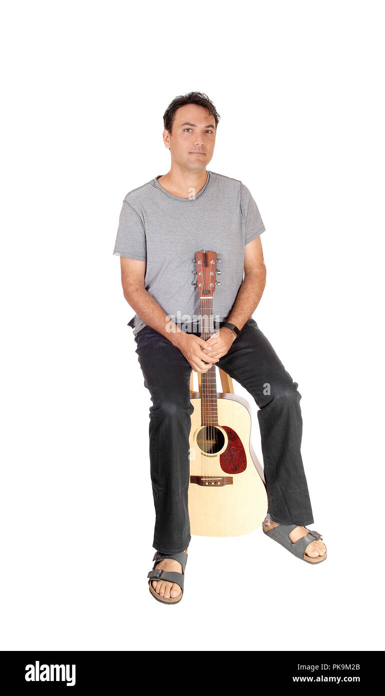 Un giovane uomo bello prendere un freno da suonare la chitarra, seduta in jeans camicia grigia e sandali, isolato per sfondo bianco Foto Stock