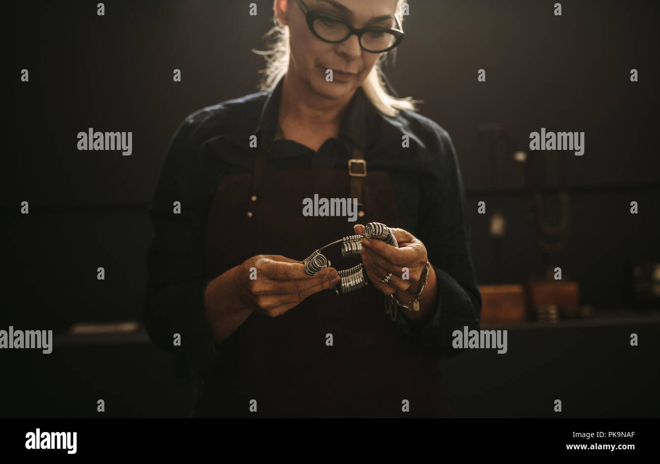 Senior donna gioielliere professionista con anello dito dosatore in officina. Femmina creatore di gioielli con calibro ad anello in officina. Foto Stock
