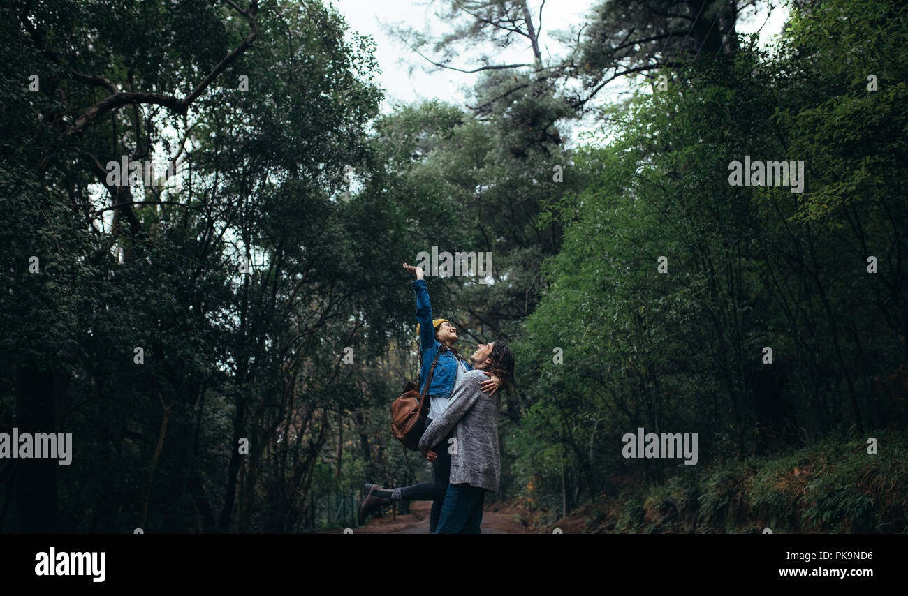 Bellissima foresta pluviale con coppia godendo. Uomo che porta la donna in armi con la donna alzando la mano e sorridente. Foto Stock