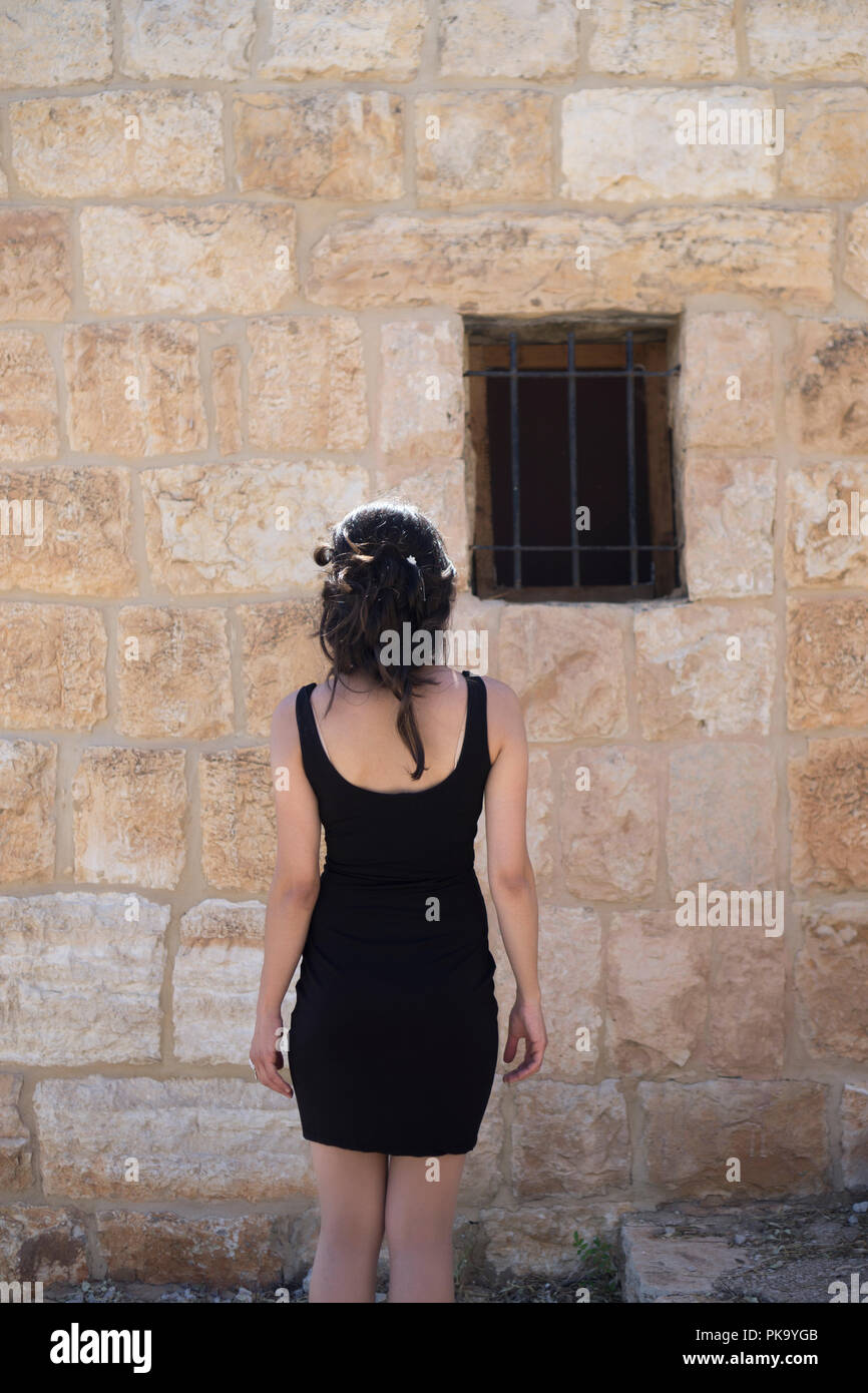 Vista posteriore di una donna che indossa un abito nero in piedi fuori casa vecchia Foto Stock