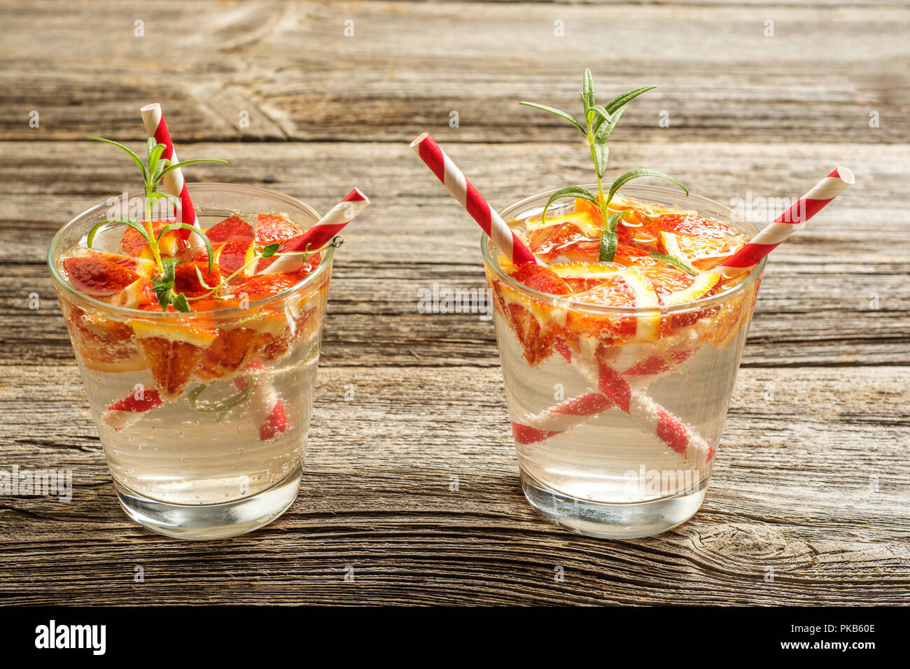 Due bicchieri di bevanda rinfrescante con arancia e rosmarino in legno rustico sfondo . Concetto di ricetta, cocktail. Foto Stock